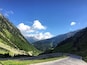 A winding mountain road surrounded by lush green hills and a clear blue sky.