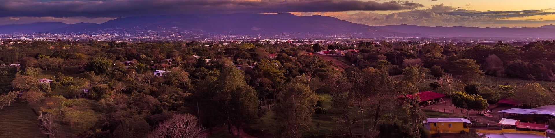 A sunset over a city with mountains in the background and a dense forest in the foreground.