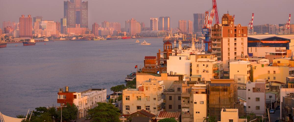 A coastal cityscape with a mix of modern skyscrapers and older buildings, a harbor with boats, and a prominent crane structure.