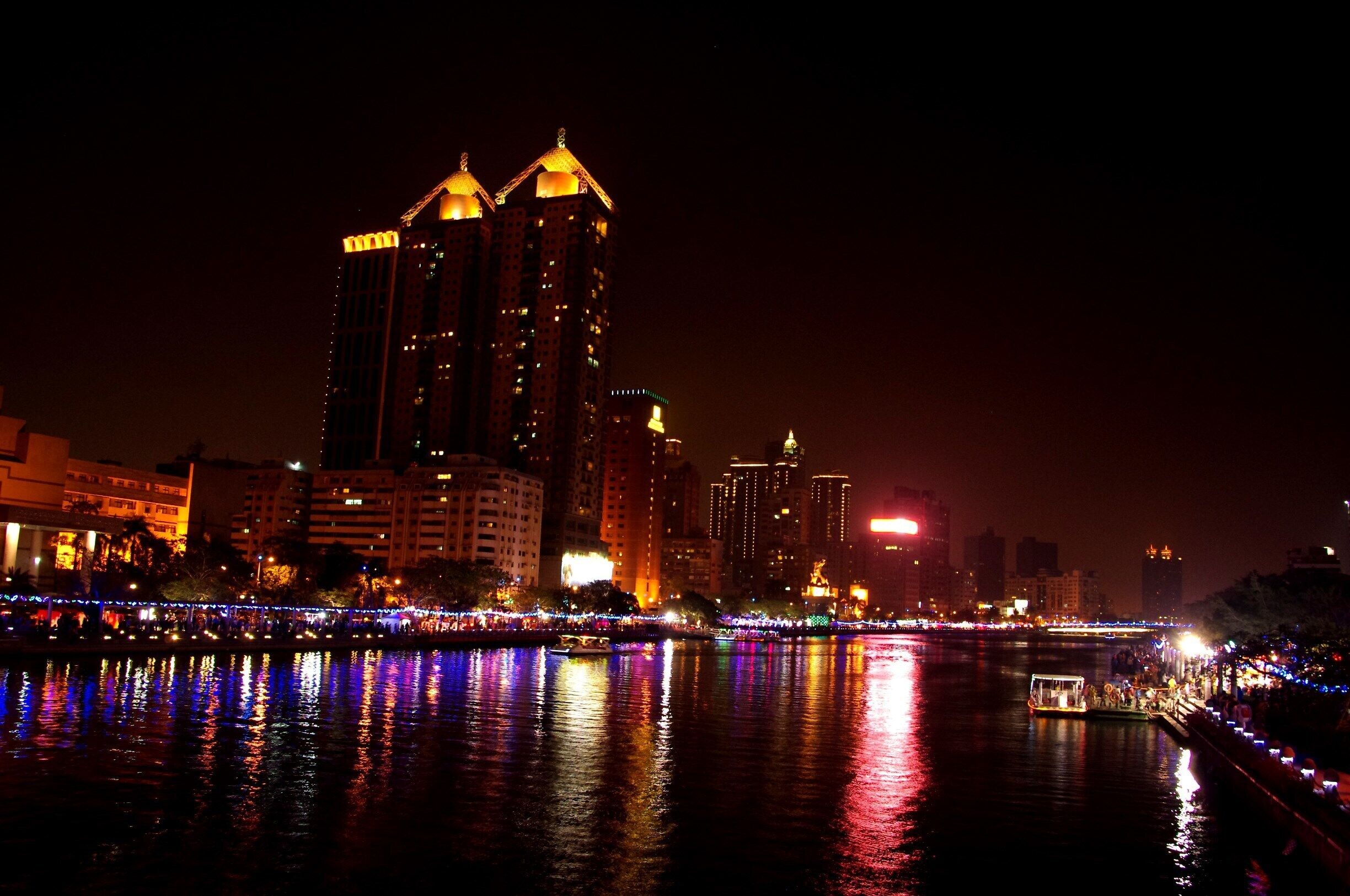 A cityscape at night with illuminated buildings and a river reflecting lights.