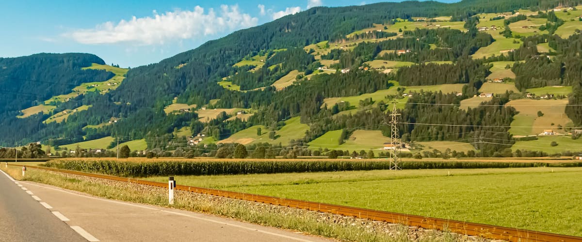 A rural landscape with a road, green fields, and a mountain range.