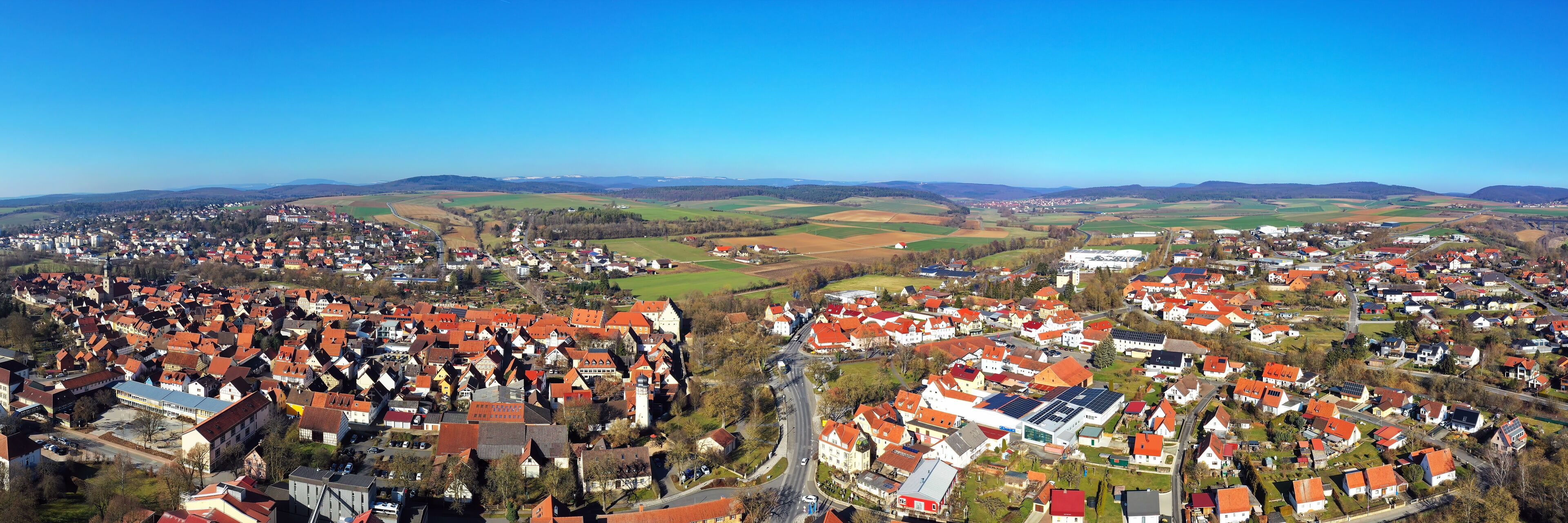 A town with red-roofed houses, a church, and surrounding fields.