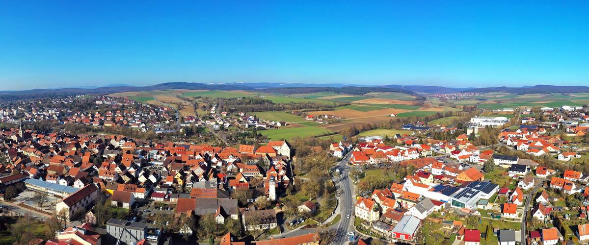 A town with red-roofed houses, a church, and surrounding fields.