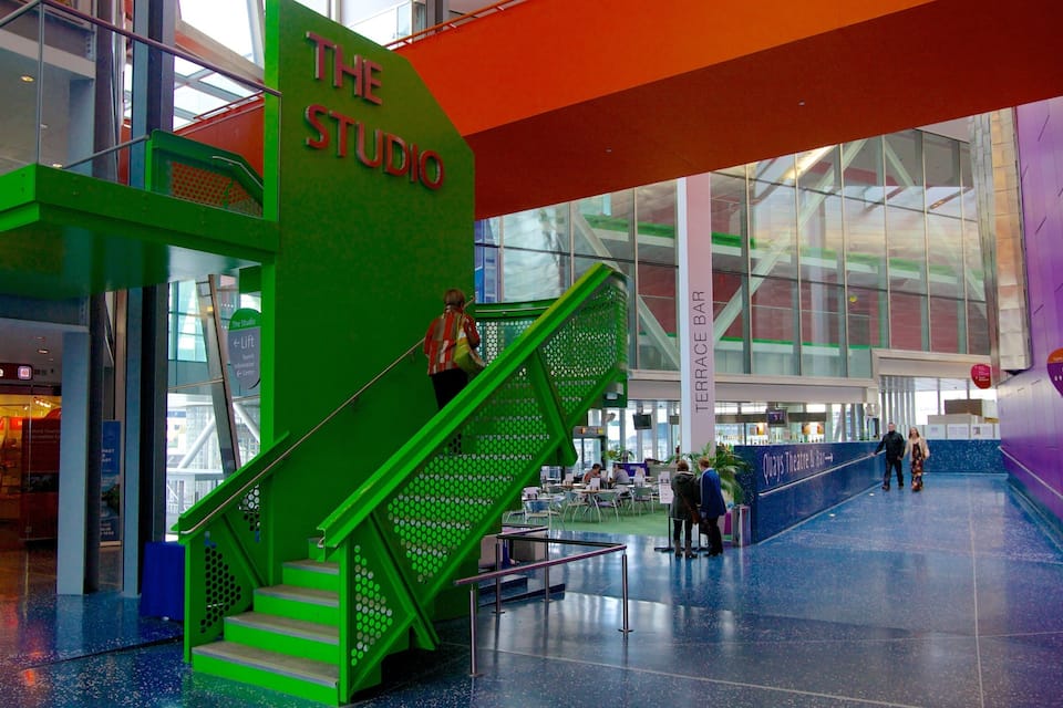 Un escalier vert mène à «
The Studio
», qui se trouve dans un bâtiment moderne aux murs de verre et au sol bleu.