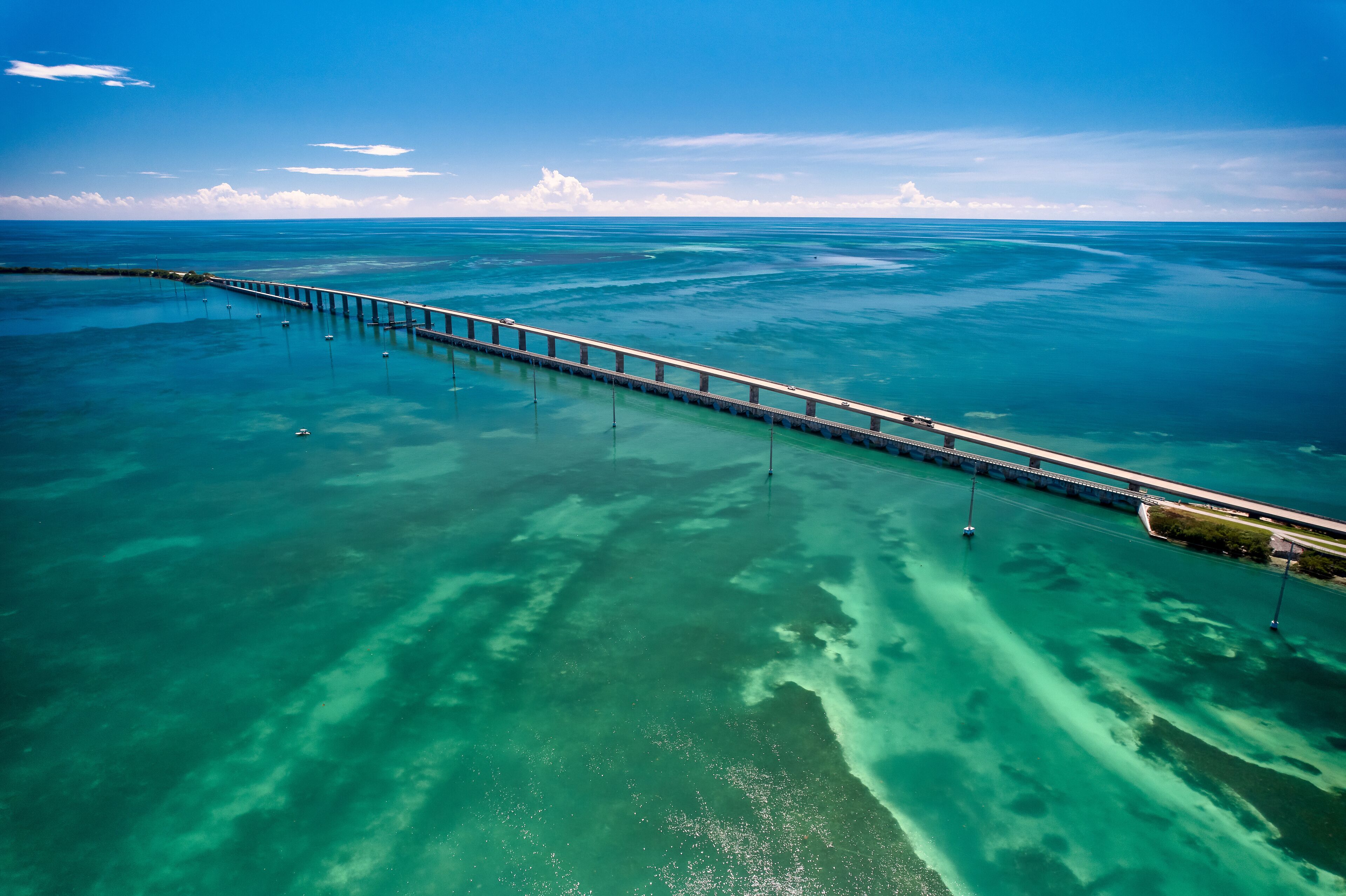 An aerial view of a long bridge over turquoise waters with clear skies.