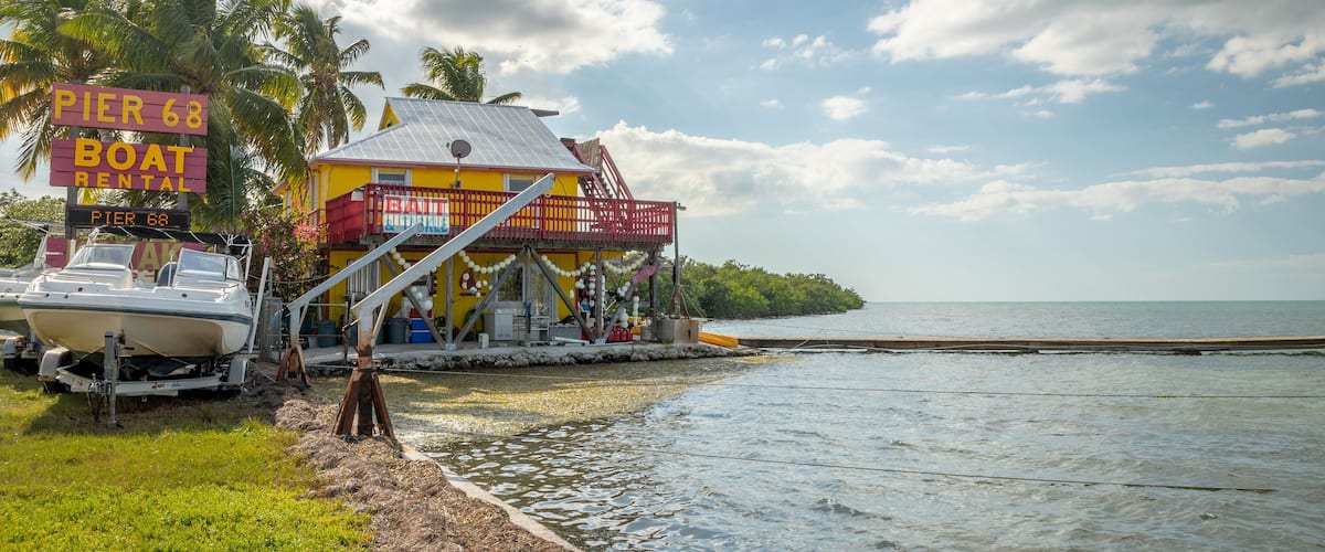 A pier with a boat rental sign, a colorful building, and a calm sea.