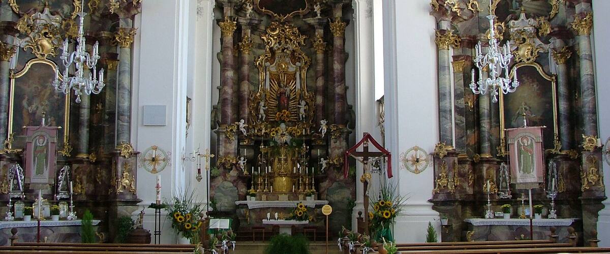 An ornate church interior with elaborate gold decorations, chandeliers, and a central altar.