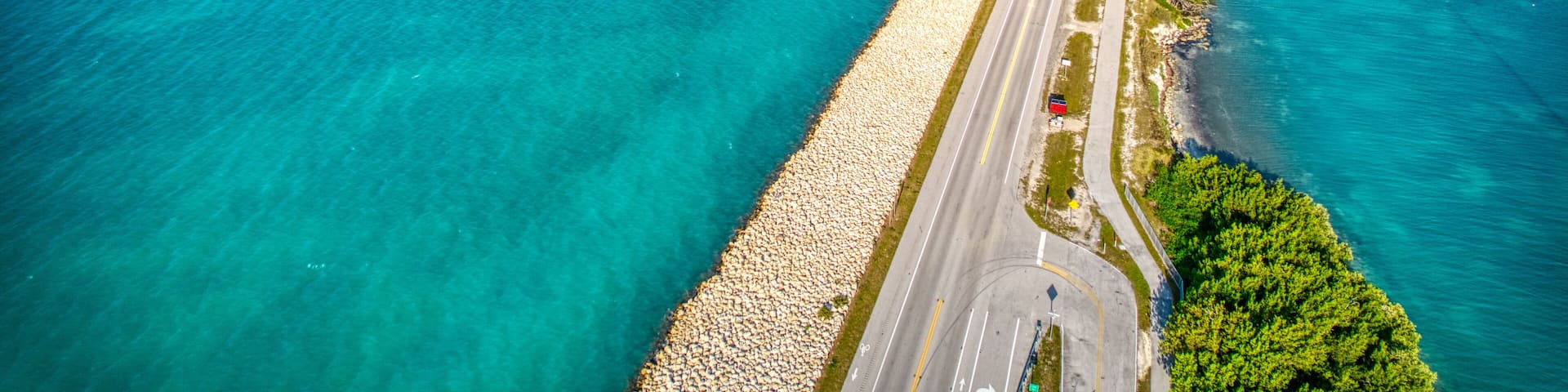 A coastal road with a beach on one side and a marina with boats on the other.
