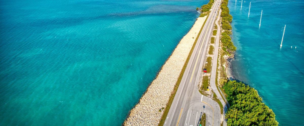 A coastal road with a beach on one side and a marina with boats on the other.