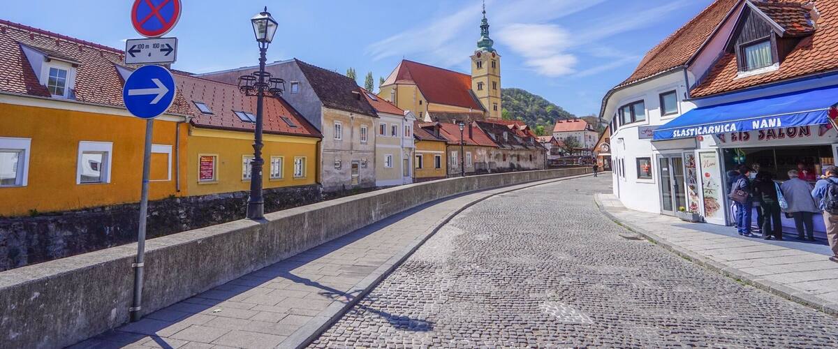 A cobblestone street with buildings, a no parking sign, and a blue directional sign.