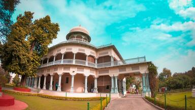 A large, ornate building with a dome and multiple balconies, surrounded by well-maintained gardens and a clear sky.