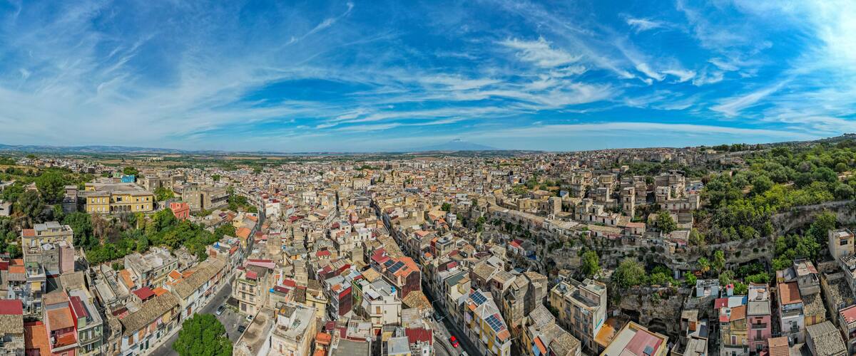 A panoramic view of a densely packed urban area with a mix of historical and modern architecture, surrounded by greenery and hills.
