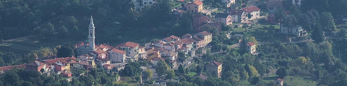 Un village perché sur une colline, avec des maisons aux toits rouges, une église dotée d’un clocher et une végétation luxuriante.