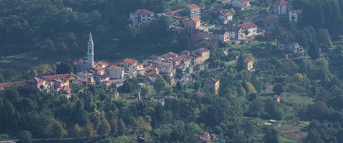 Un pueblo en una ladera con casas de tejados rojos, una iglesia con campanario y abundante vegetación.
