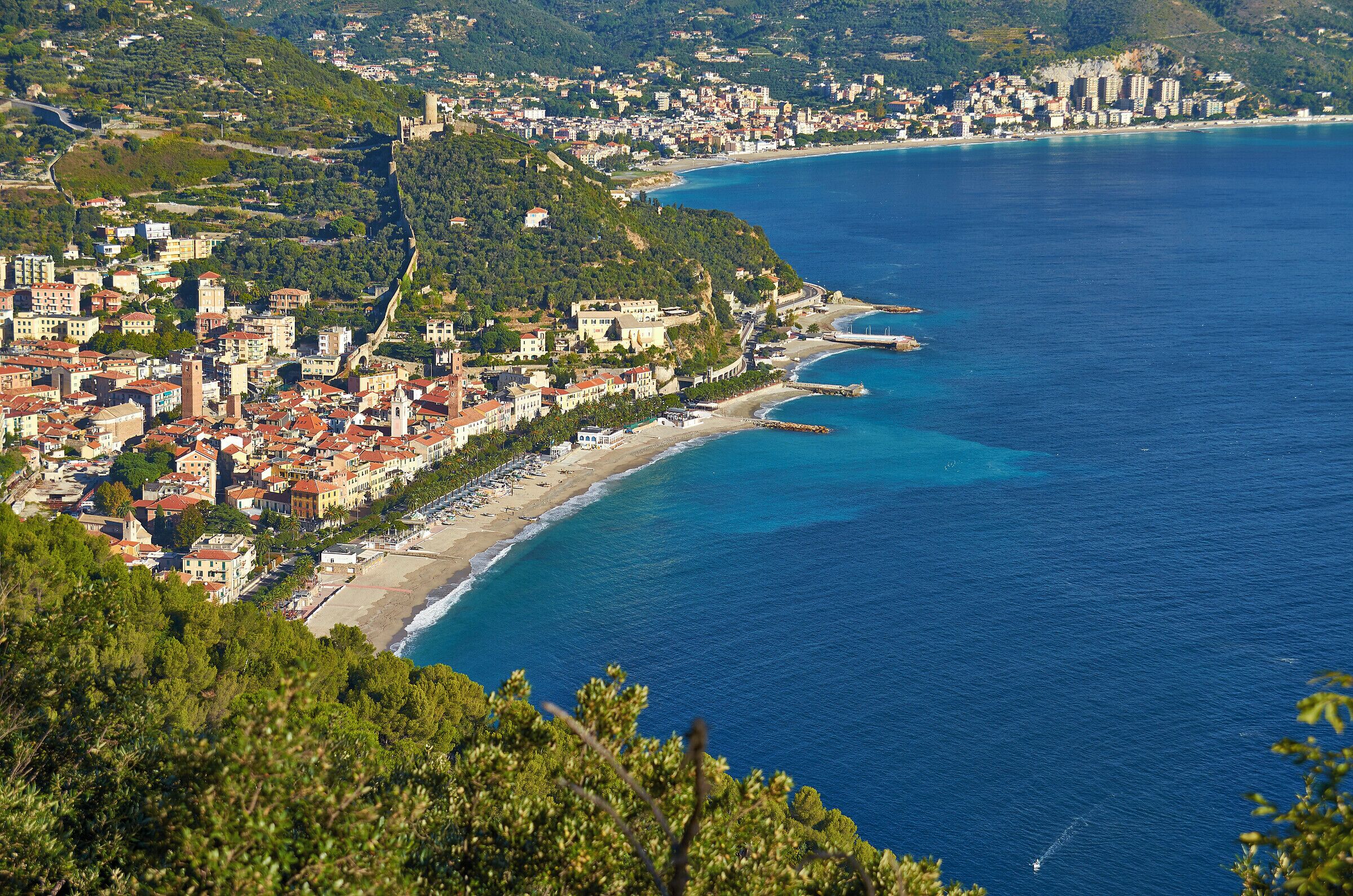 A coastal town with a beach, buildings, and a mountainous backdrop.