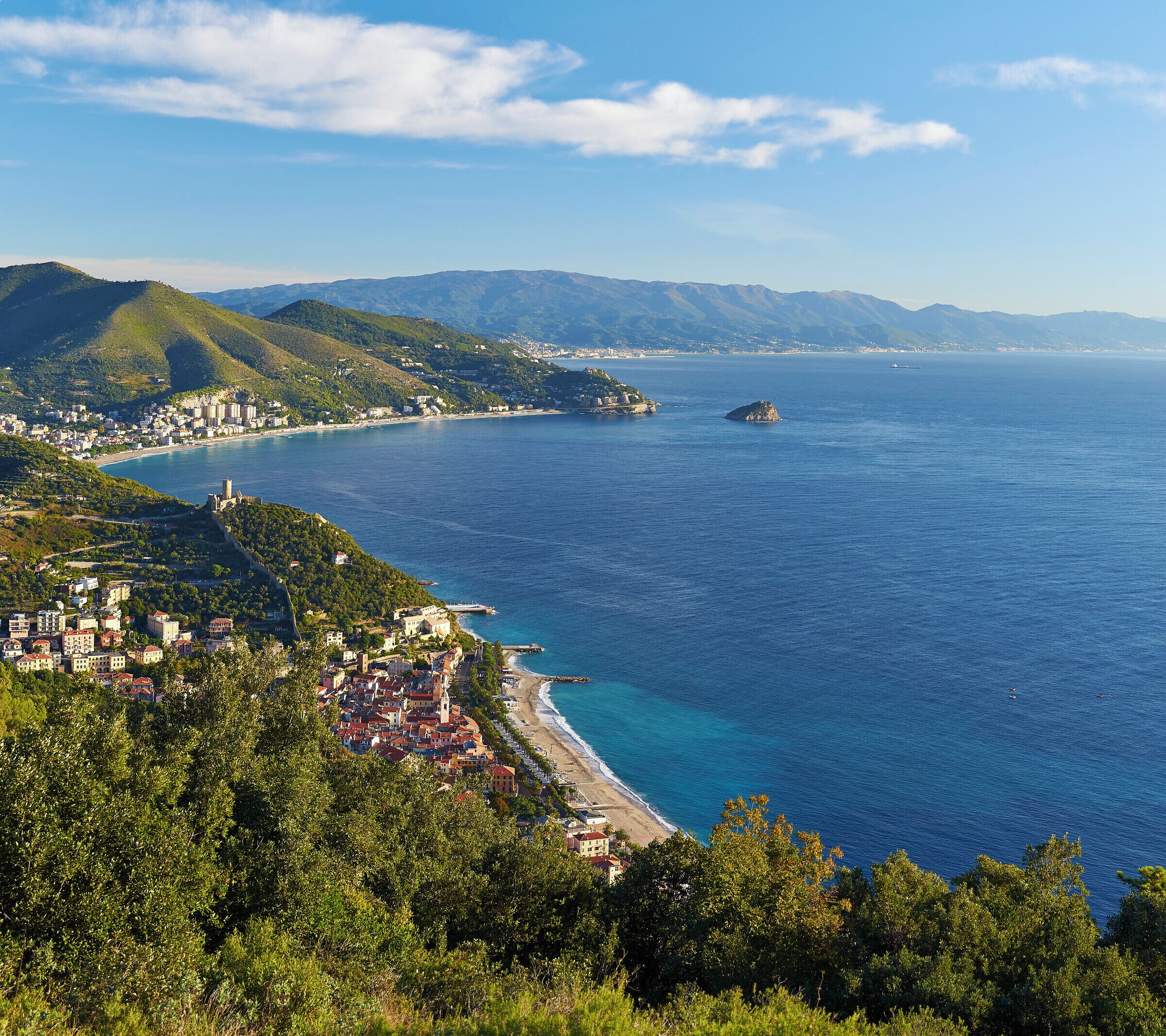 A coastal town with a beach, mountains, and a clear blue sea.