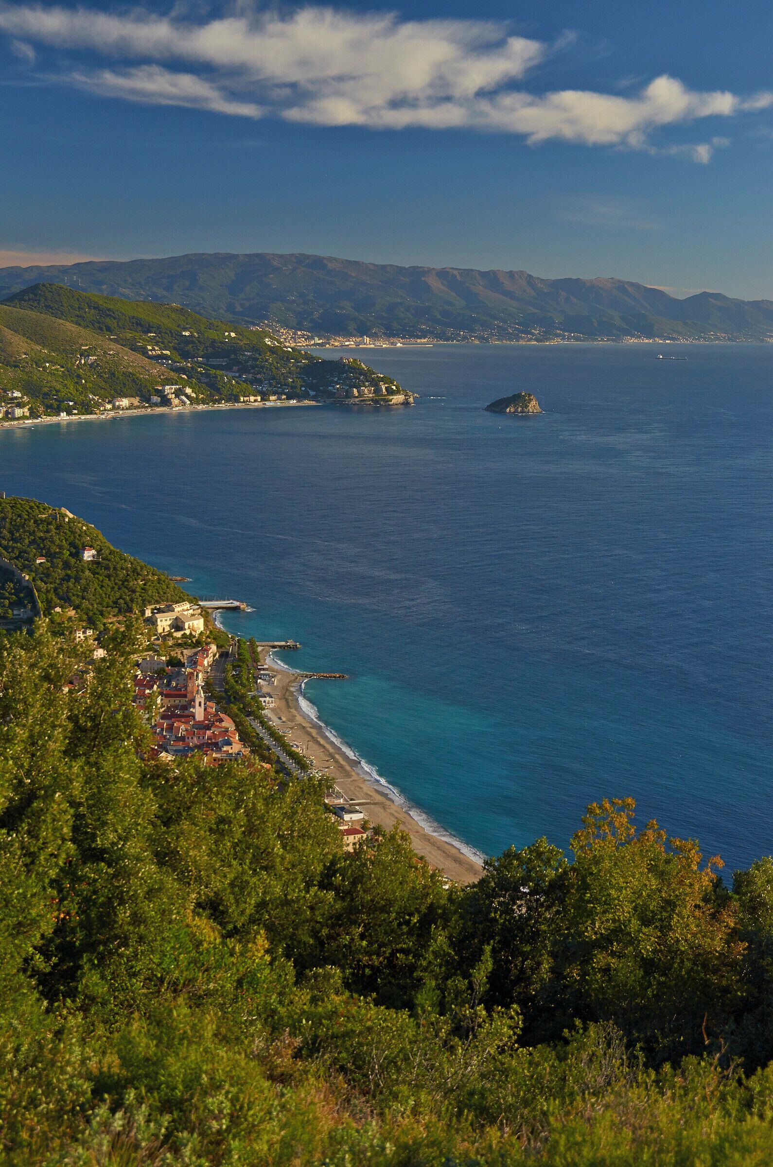 A coastal town with a beach, mountains in the background, and a clear blue sea.