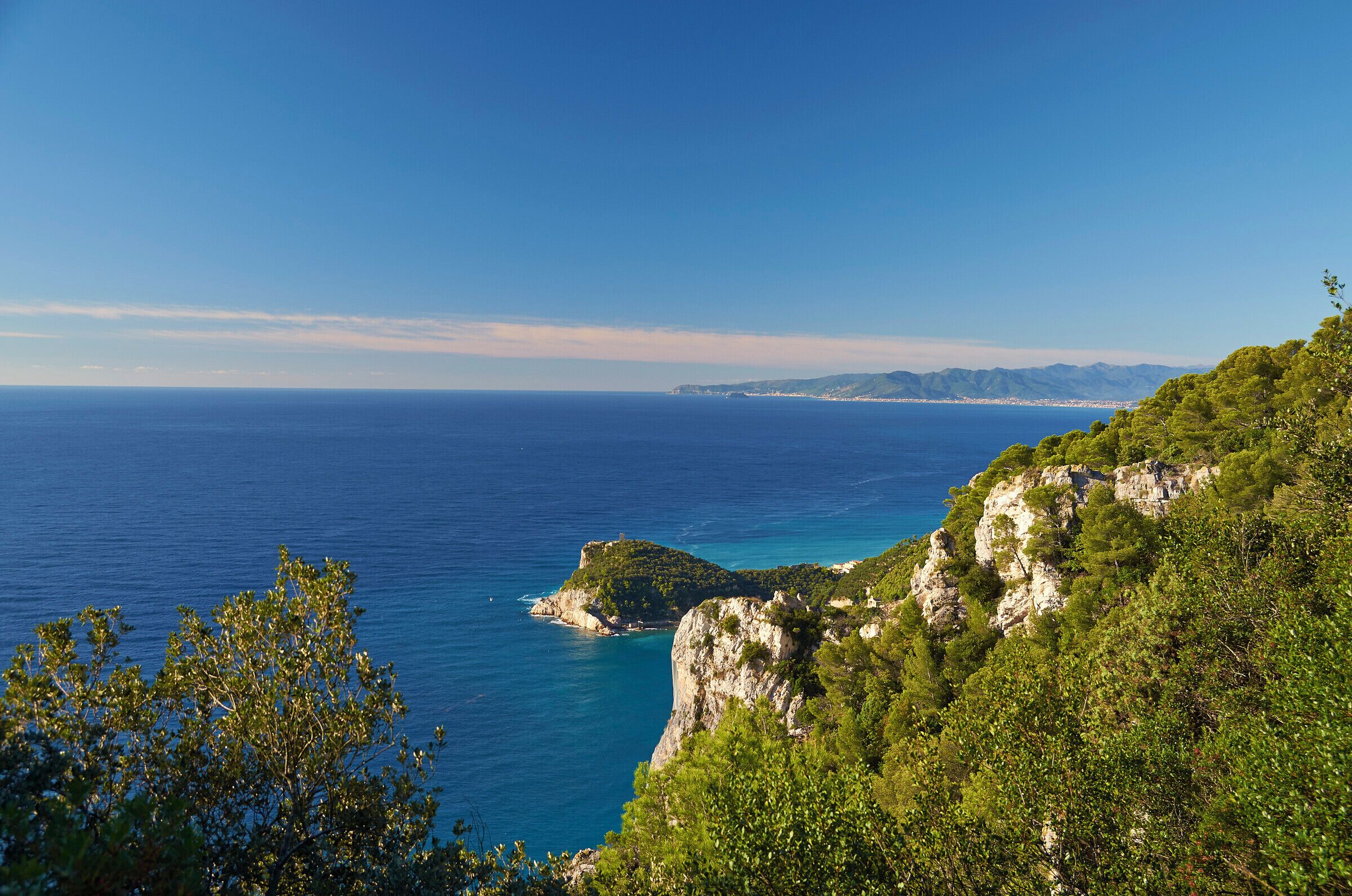 A coastal landscape with a clear blue sea, green hills, and rocky cliffs.