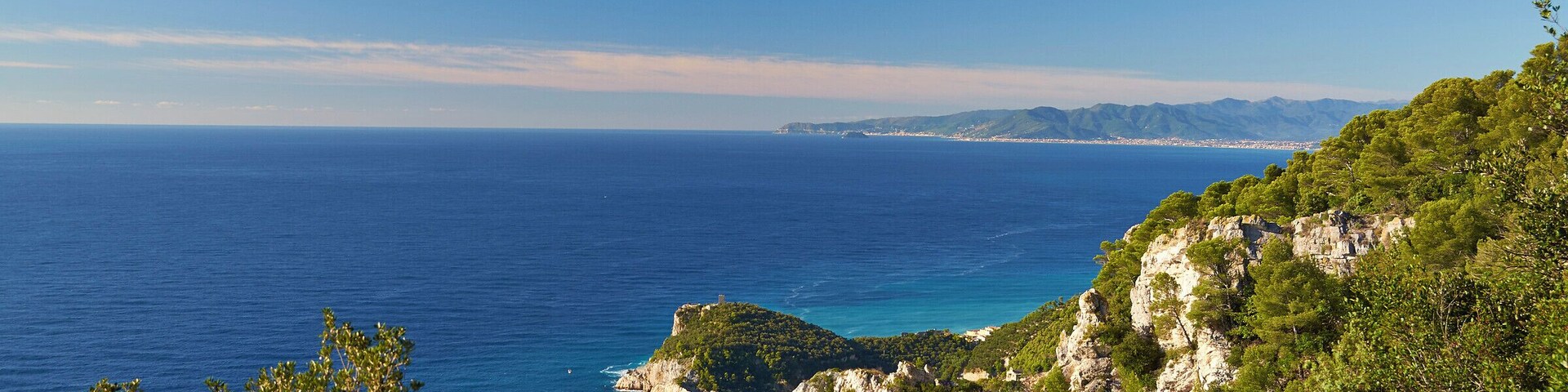 Un paisaje costero con mar azul cristalino, colinas verdes y acantilados rocosos.