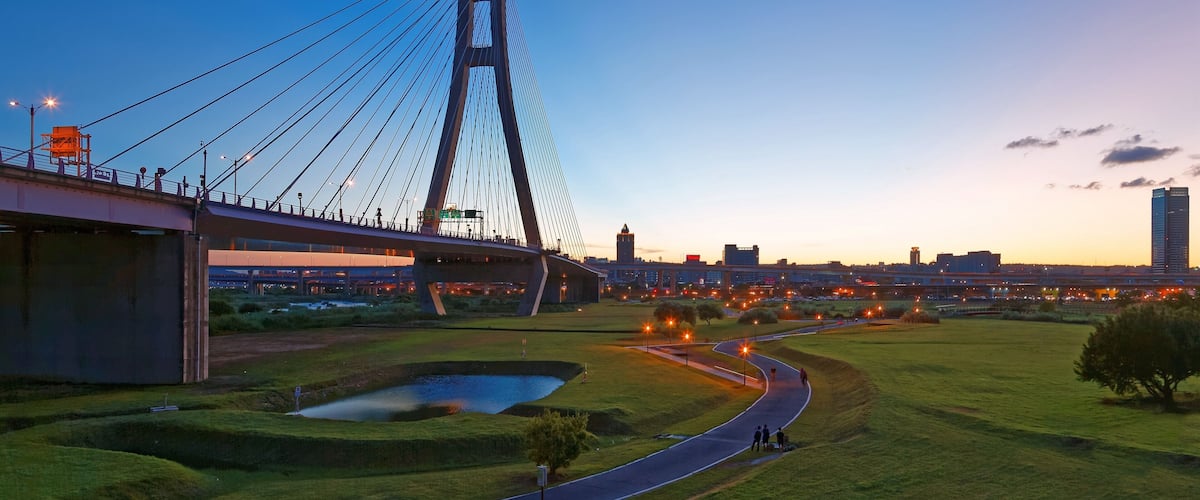 Scenery of the riverside park by Tamsui River with a pathway thru the green grassy meadow & the grand bridge tower standing tall under beautiful sunset sky in New Taipei City, Taiwan (Low Angle View )