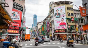 A busy urban street with various commercial signs, including a gym and a jewelry store.