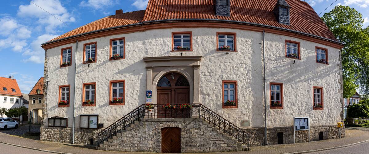A historic building with a red-tiled roof, white stucco walls, and a central arched entrance.