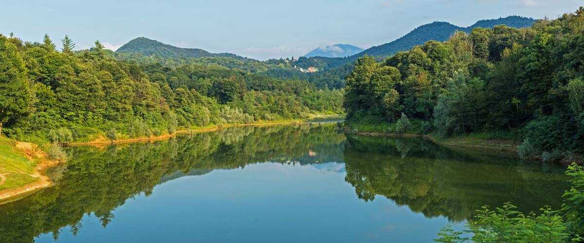 A calm river surrounded by dense forest and mountains.