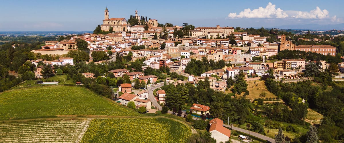 A town with a prominent church on a hill, surrounded by residential buildings and agricultural fields.