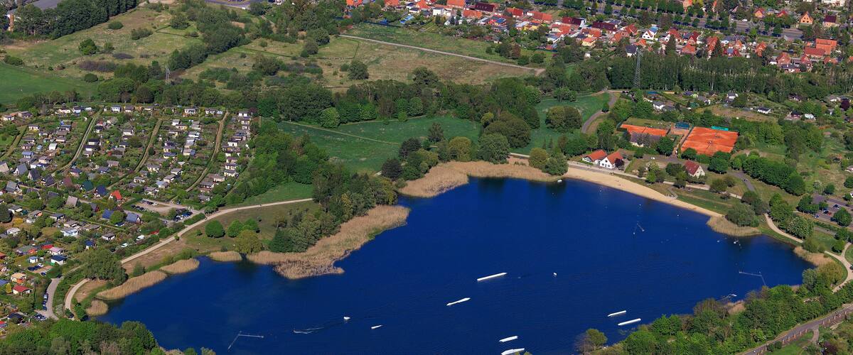 An aerial view of a lake surrounded by residential areas and dense forests.
