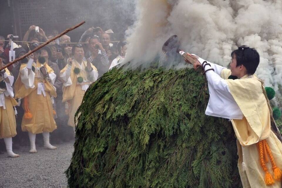 Un acte protocol·lari amb participants amb vestimentes tradicionals, una gran estructura de forma arbòria i fum.