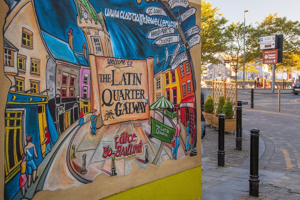 Un murale del Quartiere Latino a Galway, in Irlanda, raffigura edifici colorati e scene di strada.