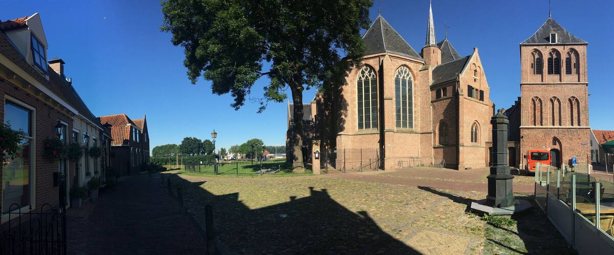 A church with a tall tower and arched windows, surrounded by cobblestone streets and trees.