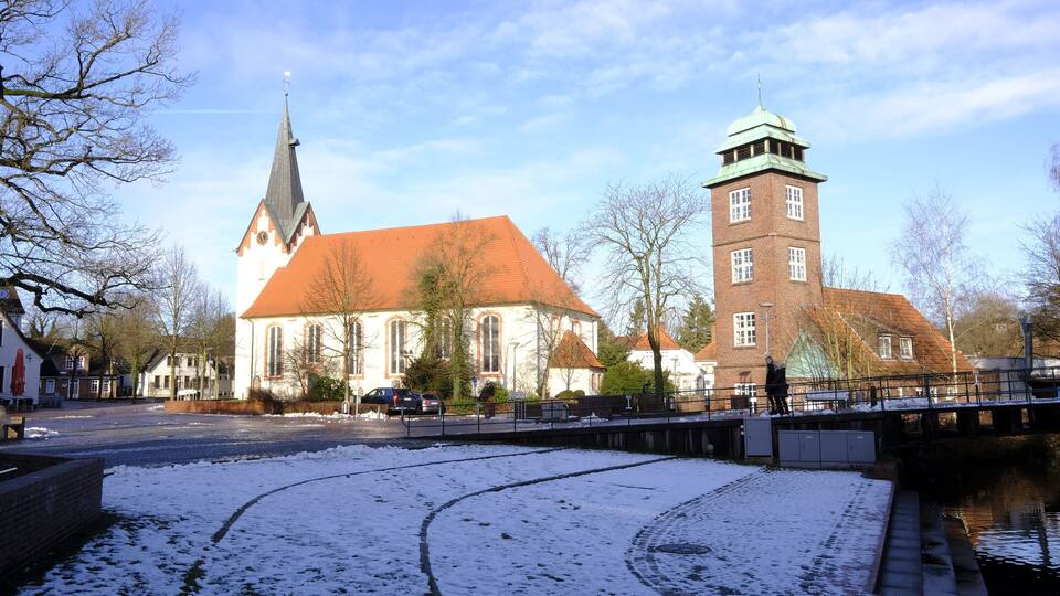 A church with a tall steeple and a clock tower, surrounded by snow-covered streets and a canal.