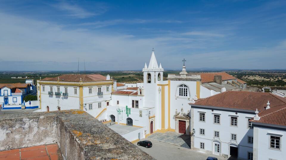 A coastal town with white buildings, a church with a bell tower, and a clear blue sky.