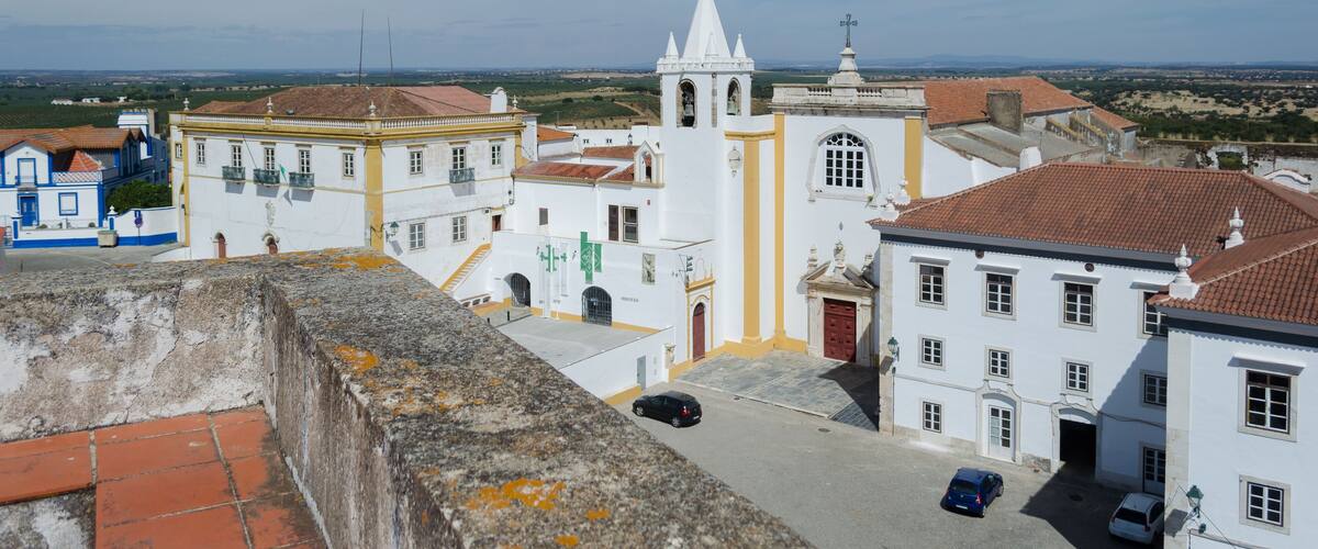 A coastal town with white buildings, a church with a bell tower, and a clear blue sky.
