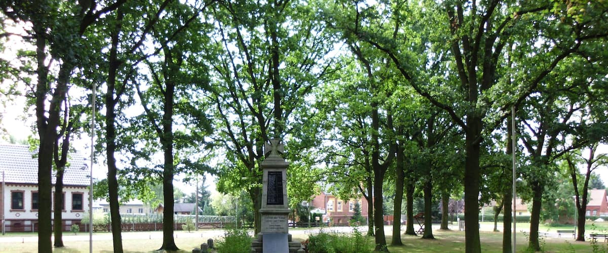 A park with a central monument, surrounded by trees and a paved walkway.