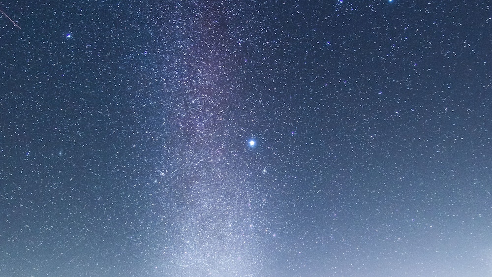A starry night sky over a forested area.
