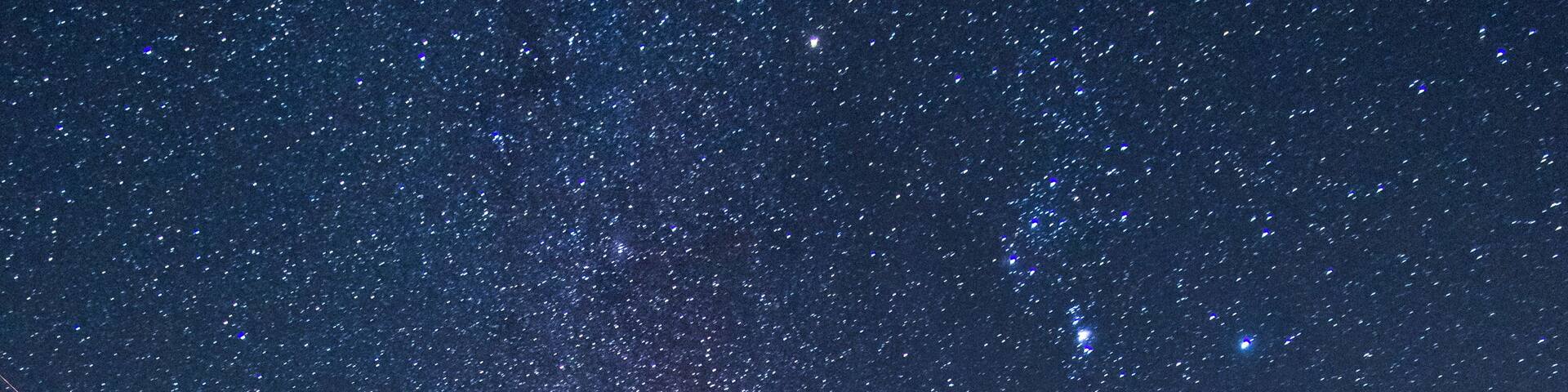 A starry night sky over a forested area.