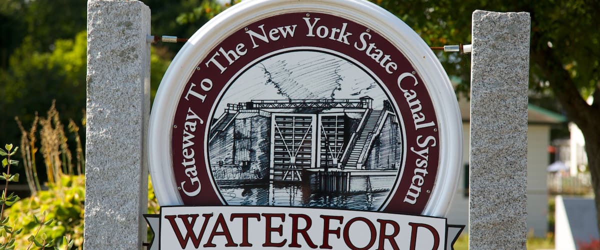 A circular sign with a historical illustration and the text "Gateway to the New York State Canal System" and "Waterford".