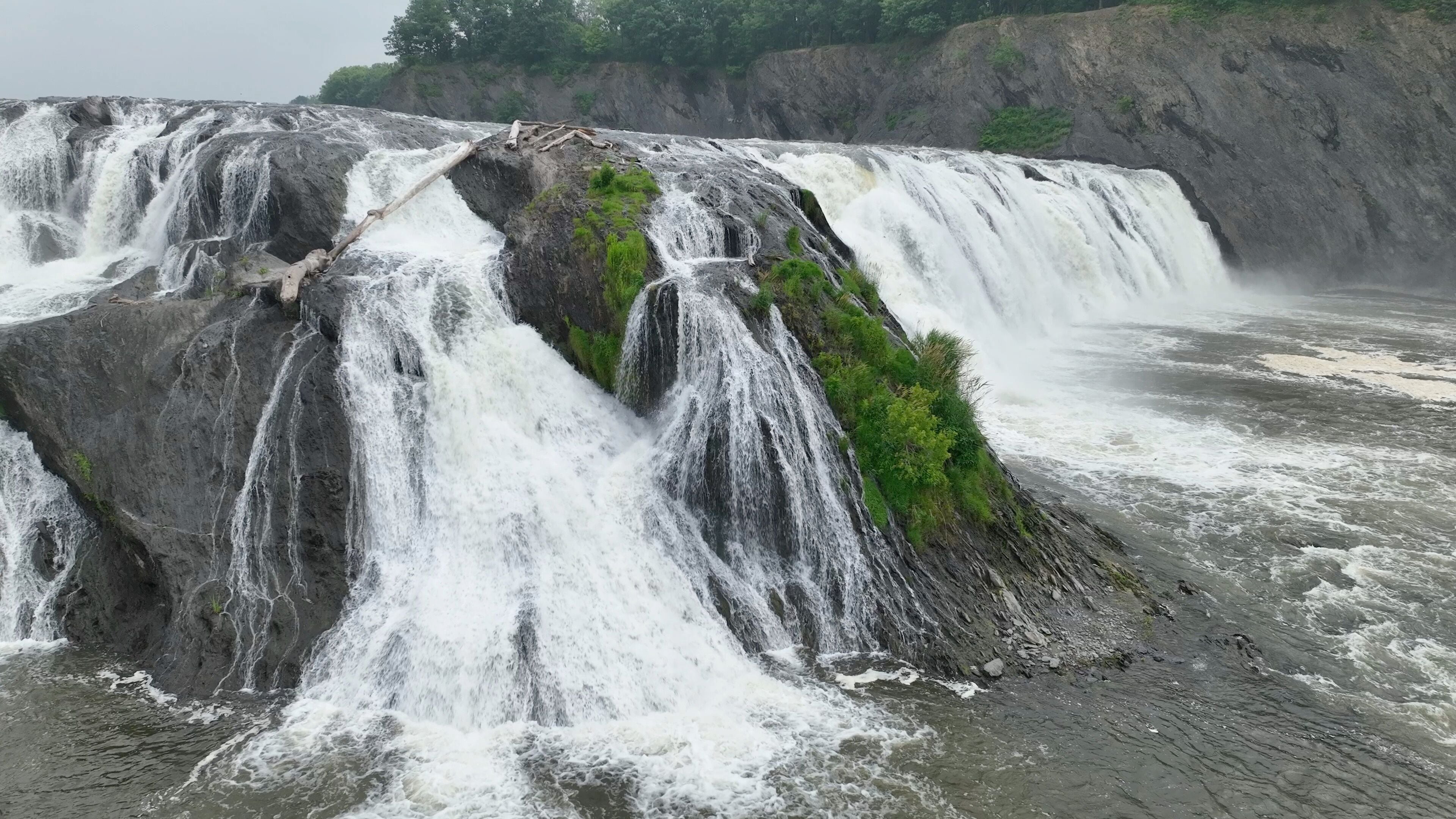 A multi-tiered waterfall with cascading water over rocky terrain and lush greenery.