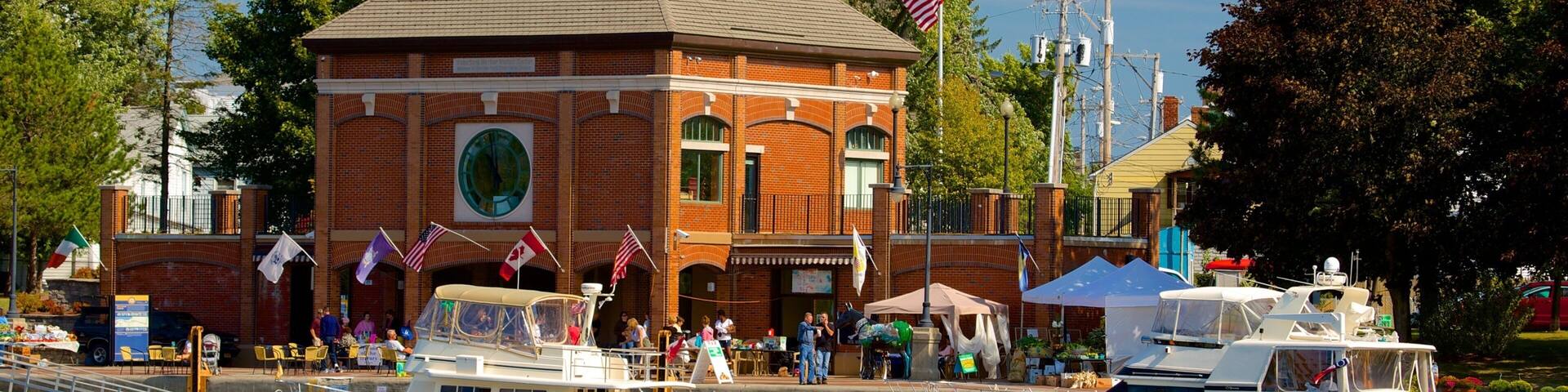 A brick building with a clock tower, a dock with boats, and flags.