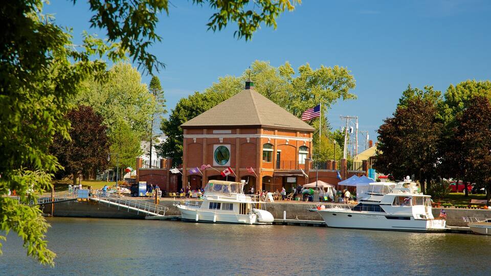 A riverside town with a prominent brick building, several boats docked, and lush greenery.
