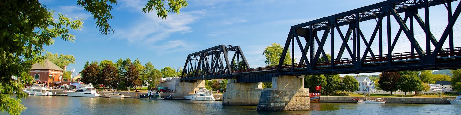 A steel bridge over a river with boats and a building in the background.
