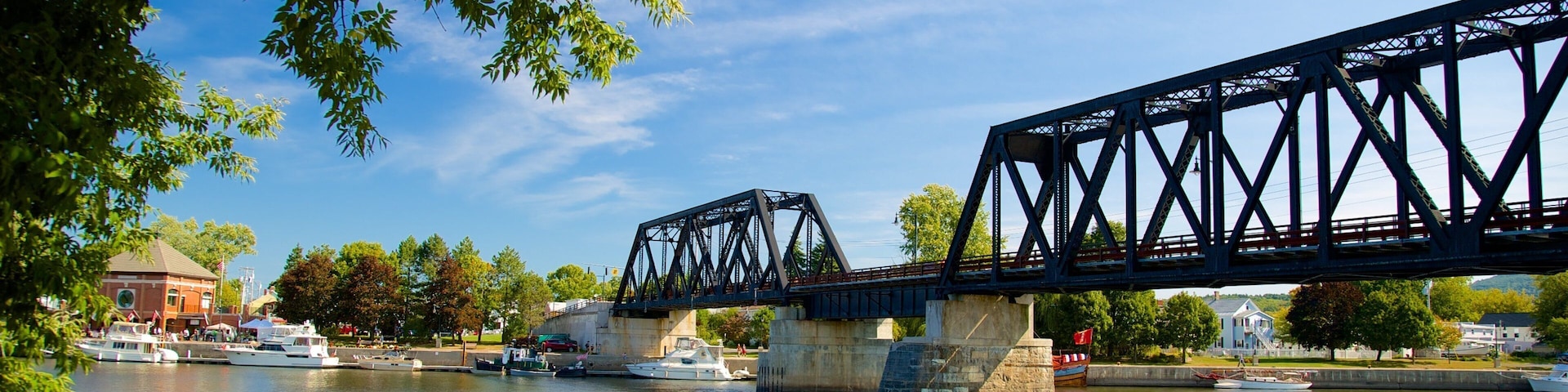 Eine Stahlbrücke über einem Fluss, mit Booten und einem Gebäude im Hintergrund.