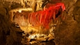 Une grotte dont les stalactites et les stalagmites sont illuminées de lumière rouge.