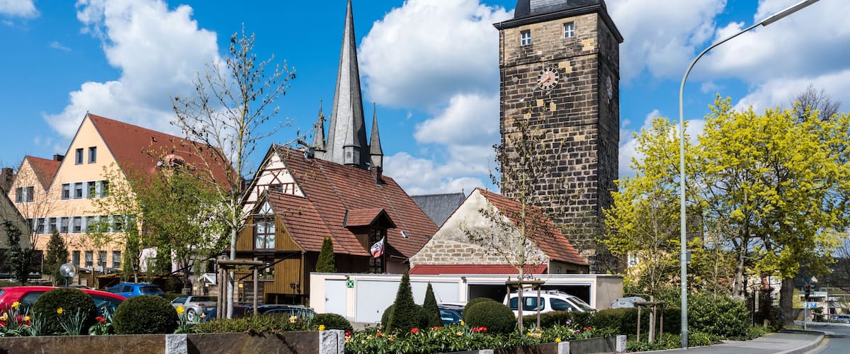 A town square with a church steeple, a clock tower, and residential buildings.