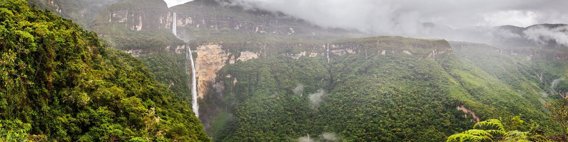 A lush green valley with a waterfall cascading down a cliff.