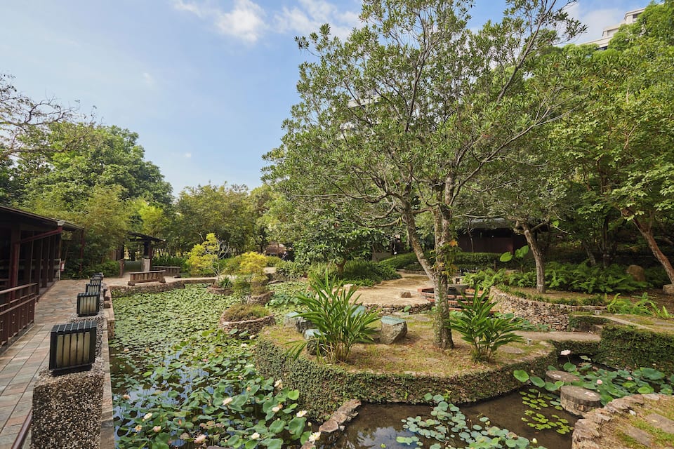 En fredfyldt have med et bassin, frodig vegetation og traditionel arkitektur.