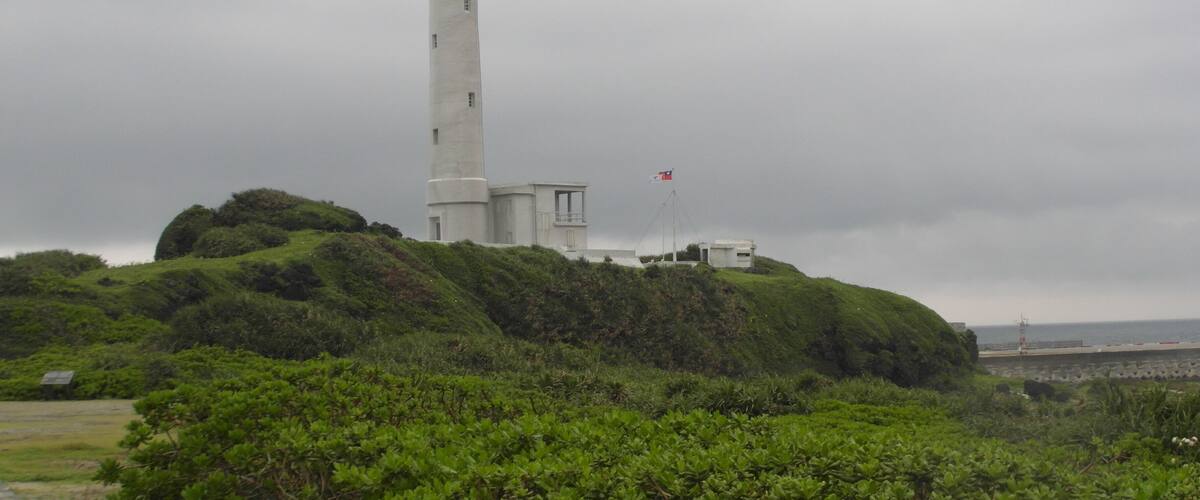 A white lighthouse on a grassy hill with a flag.