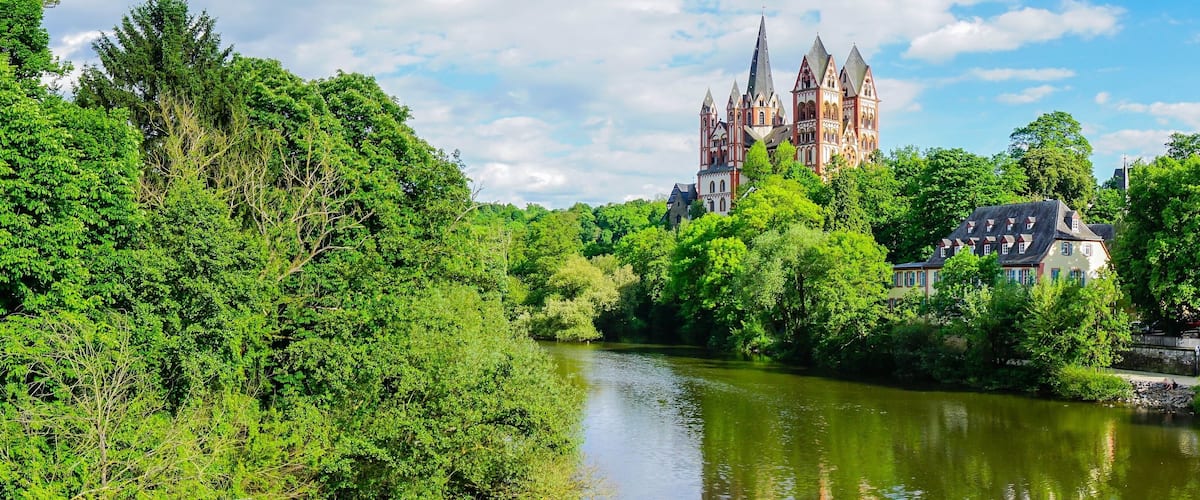 A river with lush greenery, a historic cathedral, and traditional houses.
